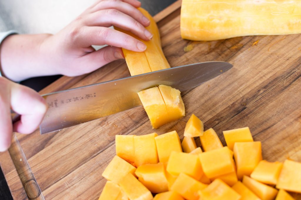 Butternut squash being diced on a wooden cutting board with a chef knife.
