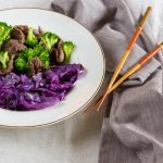 broccoli and beef in a bowl with cabbage and chop sticks