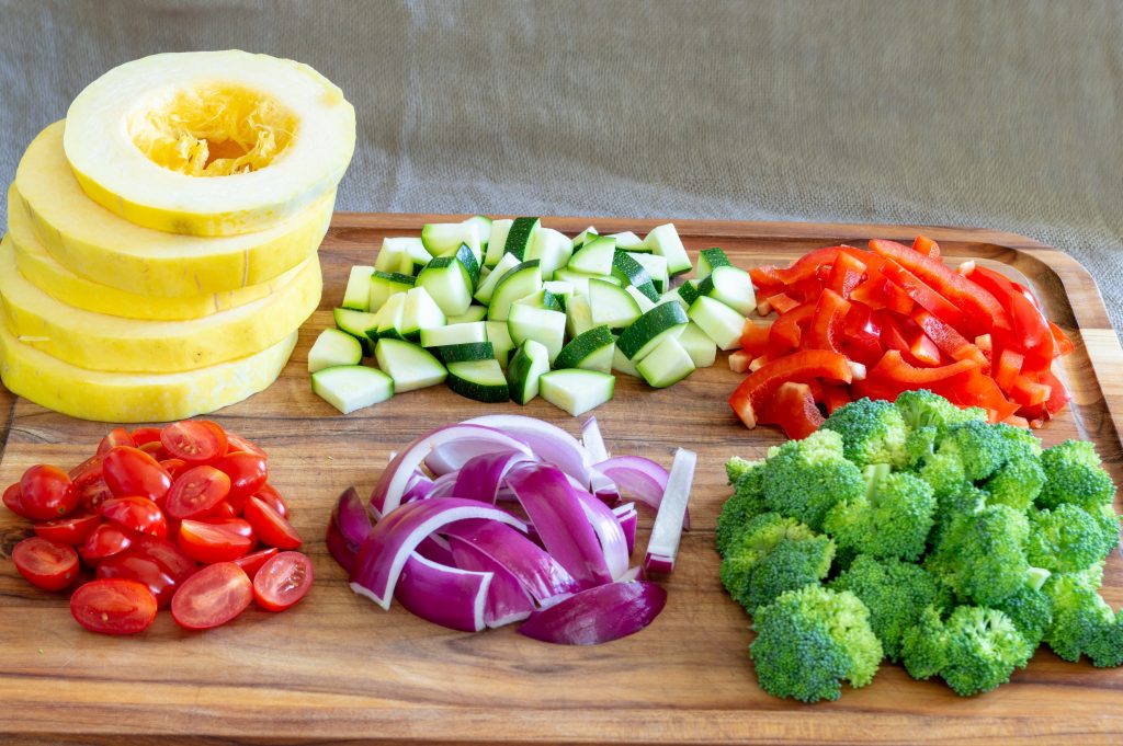 spaghetti squash, broccoli, peppers, onion, tomatoes chopped on a cutting board