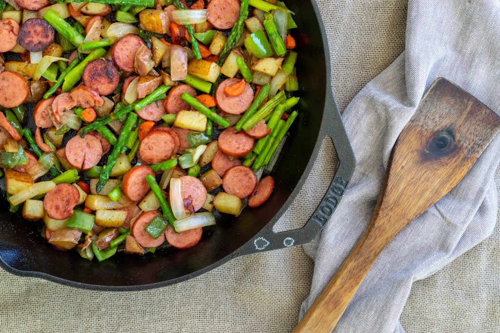 sausage and asparagus in cast iron skillet with wooden spoon
