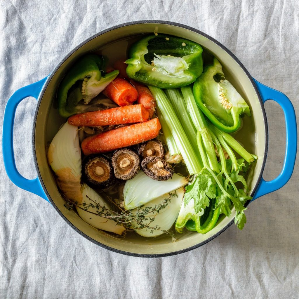blue pot with carrots, mushrooms, onion, celery and pepper in water.