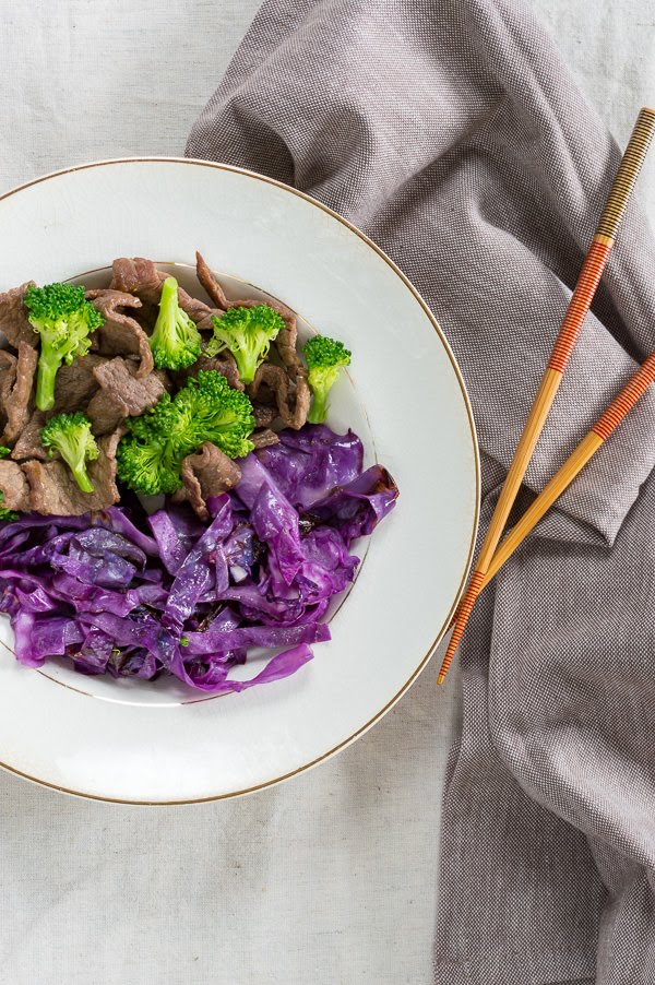 broccoli beef in a bowl with purple cabbage and chop sticks
