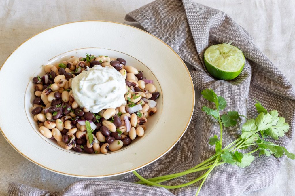 Three types of beans in a white bowl with a creamy cilantro sauce.