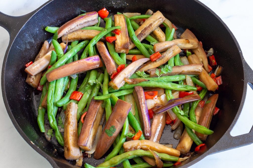 Eggplant, green beans, and red peppers in a cast iron skillet.