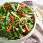 Asparagus and red pepper salad in a white salad bowl with a gray napkin and white utensils.