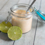 Chipotle dipping sauce in a glass jar with a spoon and lime wedges.