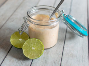 Chipotle dipping sauce in a glass jar with a spoon and lime wedges.