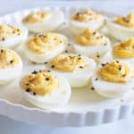 Deviled eggs with everything seasoning on a white stand with a white background.