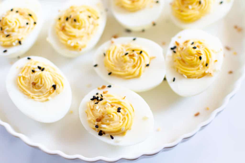 Deviled eggs with everything seasoning on a white stand.