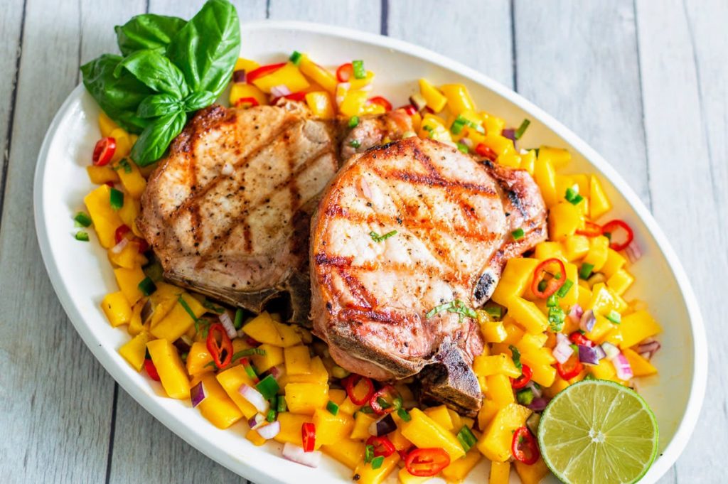 Grilled pork chops on a white plate with mango salsa.