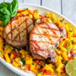 Grilled pork chops on a white plate with mango salsa.