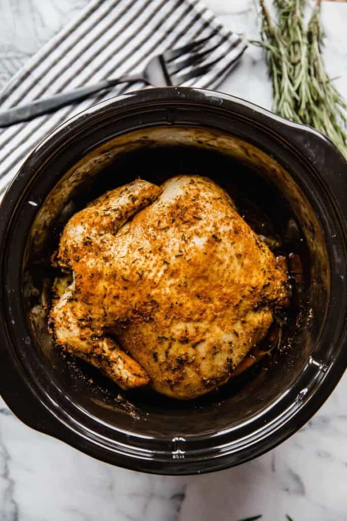 Whole chicken in a slow cooker with rosemary seasonings.
