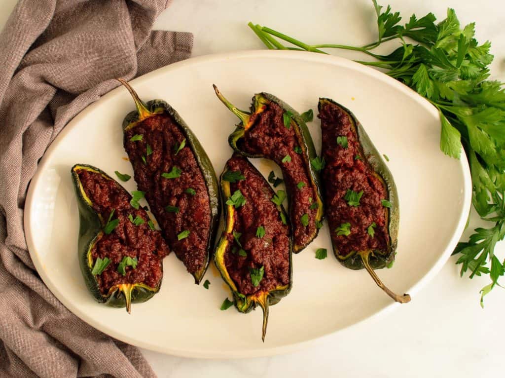 Stuffed poblano peppers on a white platter garnished with cilantro.